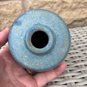 May include: A round ceramic vase with a speckled blue and light green glaze. The vase features a narrow, circular opening at the top, showcasing a textured finish with subtle variations in colour across the spherical body of the vessel.