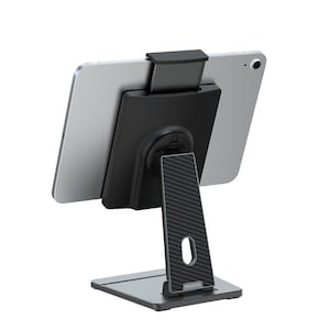 May include: A black tablet stand with a silver tablet attached. The stand has a rectangular base and a vertical support with a carbon fiber pattern. The tablet is held in place by a black bracket.