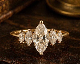 May include: A gold ring featuring a large central marquise-cut gemstone flanked by two smaller marquise-cut stones on each side. The band is thin and polished gold, showcasing a symmetrical arrangement of five clear, faceted stones in total.