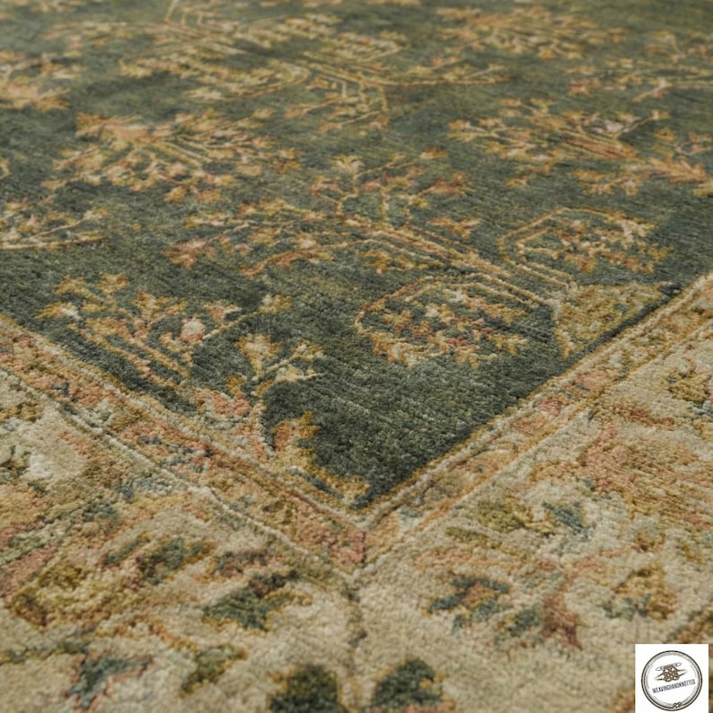 May include: Close-up of a section of a green and beige area rug. The rug features an intricate, traditional pattern with floral and geometric elements. The color palette includes shades of green, beige, and touches of pink and brown.