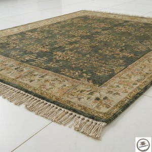May include: A rectangular area rug with a dark green center and a beige border. The rug features an intricate floral pattern in shades of beige, brown, and pink. The border has a detailed design, and the rug has fringe on the edges.