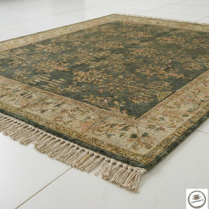 May include: A rectangular area rug with a dark green center and a beige border. The rug features an intricate floral pattern in shades of beige, brown, and pink. The border has a detailed design, and the rug has fringe on the edges.