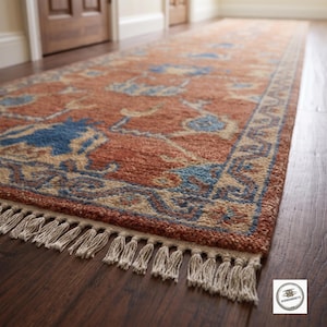 May include: A long rectangular runner rug featuring a rust-orange base color with intricate floral and geometric patterns in shades of blue and cream. The rug has a textured pile surface and is finished with cream-colored fringe along the short edge.
