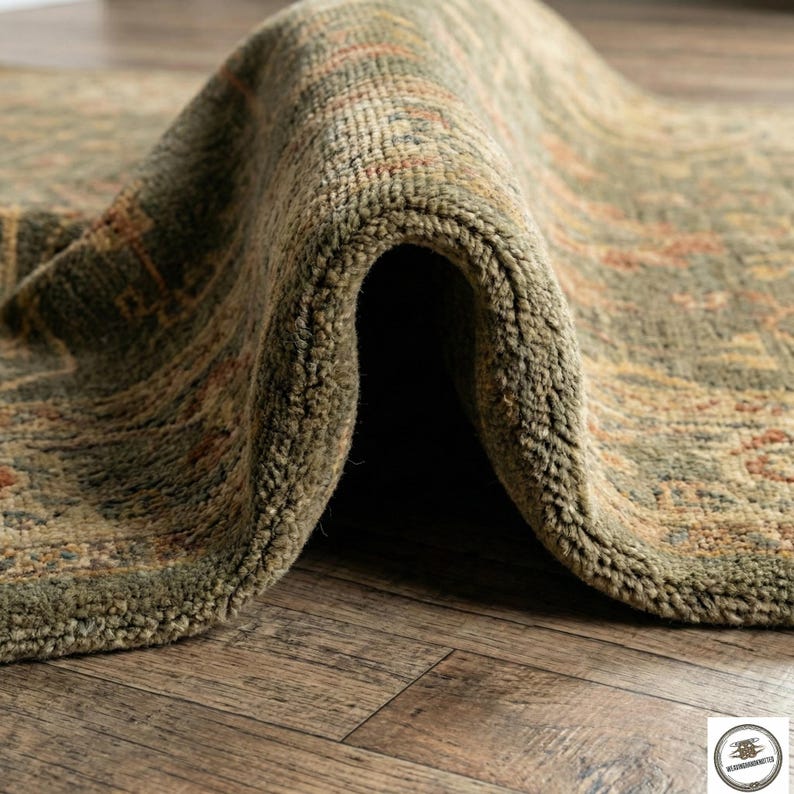 May include: Close-up of a rolled-up, olive green area rug with a distressed, patterned design. The rug's texture is visible, with a mix of olive, brown, and rust-colored details. The rug is on a wooden floor.