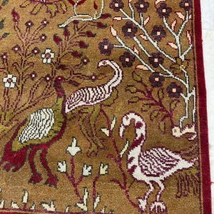 May include: A detailed, close-up view of a brown rug with a red border and fringe. The rug features a pattern of birds, flowers, and foliage in shades of red, white, green, and brown.