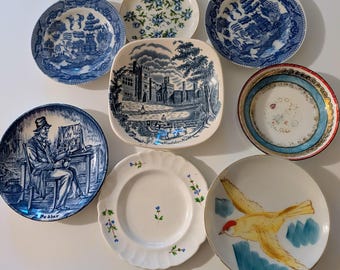 May include: A collection of eight ceramic plates featuring diverse designs including blue and white willow patterns, a square plate depicting Haddon Hall, a plate showing a pedlar, a floral plate, and a plate with a yellow bird illustration.