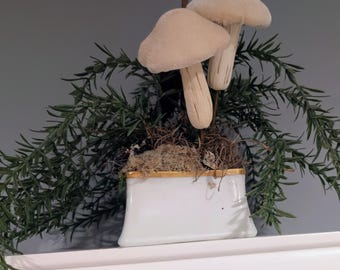 Arreglo floral artificial de setas con follaje variado en un recipiente de estilo vintage.