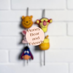 May include: A set of decorative metal garden stakes featuring colourful character heads including a yellow bear, a striped tiger, a pink rabbit, a blue donkey, and a yellow honey pot. The text Honey Bear and Friends is centred on the image.