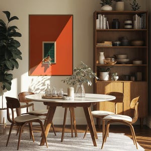 May include: A dining room featuring a round white table with wooden legs, four wooden chairs with white cushions, and a tall wooden bookshelf. On the wall hangs a large framed print of a person playing a guitar in a window against an orange wall.
