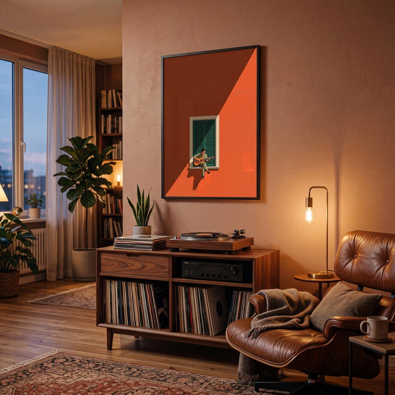 May include: A framed wall art print featuring a minimalist illustration of a person sitting on a window ledge playing an acoustic guitar, set against a vibrant orange wall with green shutters, displayed in a black frame on a warm-toned wall.