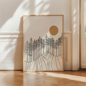 May include: A rectangular wall art print in a light wood frame featuring a black line drawing of a forest of pine trees on a rolling hill against a cream background with a solid gold circle representing the sun positioned in the upper right corner.