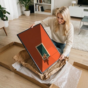 May include: A rectangular framed wall art print featuring a vibrant orange wall with a central window that has green shutters. A person is sitting on the window ledge playing an acoustic guitar, casting a long shadow on the orange surface.