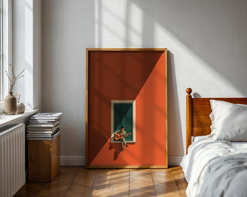 May include: A rectangular framed wall art print featuring a solid burnt orange background with a centered window. The window has dark green louvered shutters and a small figure sitting on the sill playing an acoustic guitar, casting a shadow.