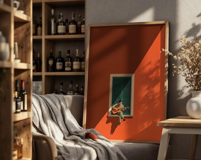 May include: A framed rectangular wall art print featuring a solid burnt orange background with a centered green shuttered window. A small figure sits on the window ledge playing an acoustic guitar, casting a distinct shadow on the orange wall.