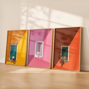 May include: Three rectangular framed wall art prints featuring minimalist architectural scenes. Each print displays a person sitting on a window ledge against a solid color background divided diagonally by light and shadow, in yellow, pink, and orange.
