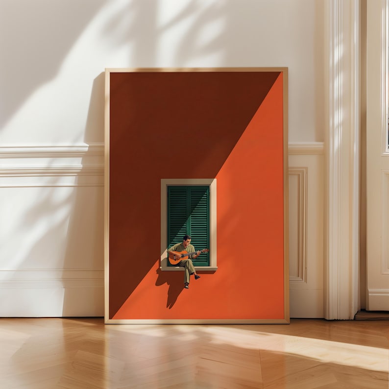 May include: A framed rectangular wall art print featuring a person sitting on a window ledge playing an acoustic guitar. The scene depicts a dark green shuttered window set against a solid terracotta orange wall with sharp diagonal shadows.