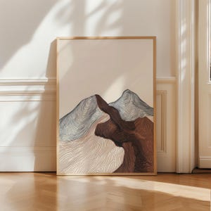May include: A framed art print depicting a minimalist mountain scene. The artwork uses a line drawing technique with brown, grey, and beige tones. The print is presented in a light wood frame, offering a contemporary feel.