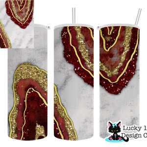 May include: A stainless steel tumbler with a geode design. The design features red and gold glitter accents on a grey background. The tumbler includes a silver straw and a white lid. The Lucky 13 Design Co. logo is visible.