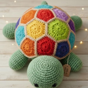 Peut inclure: Une tortue crochetée à la main avec une carapace multicolore. La carapace est composée de plusieurs couleurs, dont le rouge, l'orange, le jaune, le vert, le bleu et le violet. La tête, les nageoires et la queue sont vertes. Une étiquette indique "handmade by sarah".