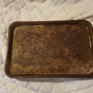 May include: A rectangular, brown resin tray with a glittery, speckled design. The tray has rounded corners and a raised edge. The glitter includes various colors, adding a touch of sparkle to the tray's surface.