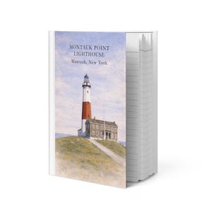 Op de afbeelding: Een notitieboek met een aquarel schilderij van de Montauk Point Lighthouse in Montauk, New York. De vuurtoren is wit met een rode top, tegen een blauwe lucht. De tekst "MONTAUK POINT LIGHTHOUSE Montauk, New York" staat op de kaft.