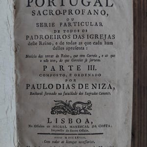 May include: An antique book, open to a page with Portuguese text. The title "PORTUGAL SACRO-PROFANO" is visible in bold, black lettering. The aged paper has a slightly yellowed hue, and the text details church information.