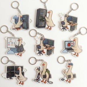 May include: A collection of acrylic keychains featuring a cartoon goose in various IT-related scenarios. The goose is depicted with server racks, computers, and the word "BUG" on a magnifying glass. Each keychain has a silver metal ring.