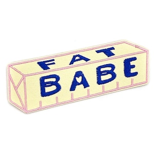 May include: Embroidered patch in the shape of a butter stick with the words "FAT BABE" in blue letters. The patch has a light yellow background with pink outlines and details.