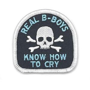 May include: A black patch with a white skull and crossbones design. The patch has the words "REAL B-BOYS" and "KNOW HOW TO CRY" in light blue lettering. The patch is bordered with white stitching.