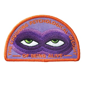 May include: Embroidered patch with a purple mask design and the text "THE CRUSHING PSYCHOLOGICAL WEIGHT OF BEING ALIVE" in orange and white. The patch features green eyes and an orange border.