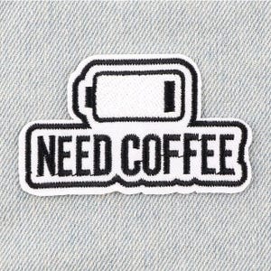 May include: A white patch with black border and text that reads "NEED COFFEE". The patch features a battery icon with a low charge. The patch is likely an iron-on or sew-on patch for clothing or accessories.