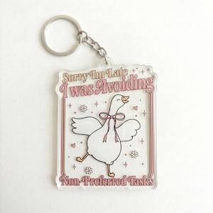 May include: A clear acrylic keychain with a cartoon goose illustration. The goose has a pink bow and is running. The keychain has the text "Sorry Im Late I was Avoiding Non-Preferred Tasks" in pink and white.