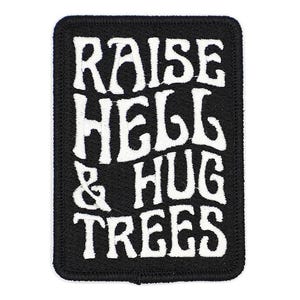 May include: Black rectangular patch with white embroidered text that reads "RAISE HELL & HUG TREES". The patch has a black border and is likely designed to be sewn or ironed onto clothing or accessories.
