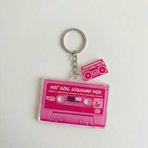 May include: A pink cassette tape keychain with the text "HOT GIRL HIGHWAY MIX" and "Vibes in overdrive, drama in the rearview mirror." A small pink boombox charm and a silver key ring complete the design.