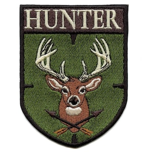 May include: Embroidered patch featuring a deer head with large antlers and crossed arrows. The word "HUNTER" is stitched across the top in a brown font. The patch has a green background and a black border.