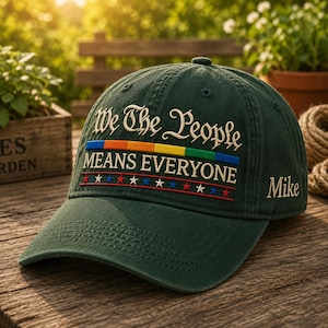 May include: A dark green baseball cap featuring the embroidered text "We The People" in white, followed by a horizontal rainbow stripe, the text "MEANS EVERYONE" in white, and a row of small red, white, and blue stars. The name "Mike" is on the side.