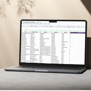 May include: A laptop displaying a spreadsheet titled "Travel Card Perks Tracker." The screen shows a table with columns for card, reward/credit, amount, frequency, category, and next available date. The laptop is open on a light-colored surface.