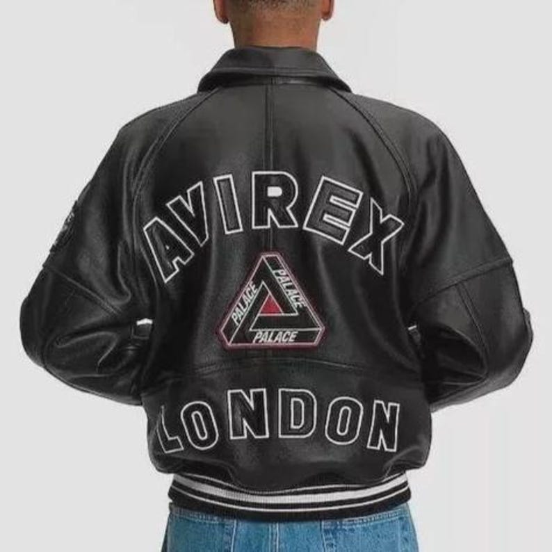 Puede incluir: Chaqueta de cuero negra con la palabra "AVIREX" en letras blancas, sobre un tri&aacute;ngulo rojo y negro con la palabra "PALACE". La palabra "LONDON" est&aacute; debajo. La chaqueta tiene cuello y pu&ntilde;os a rayas.