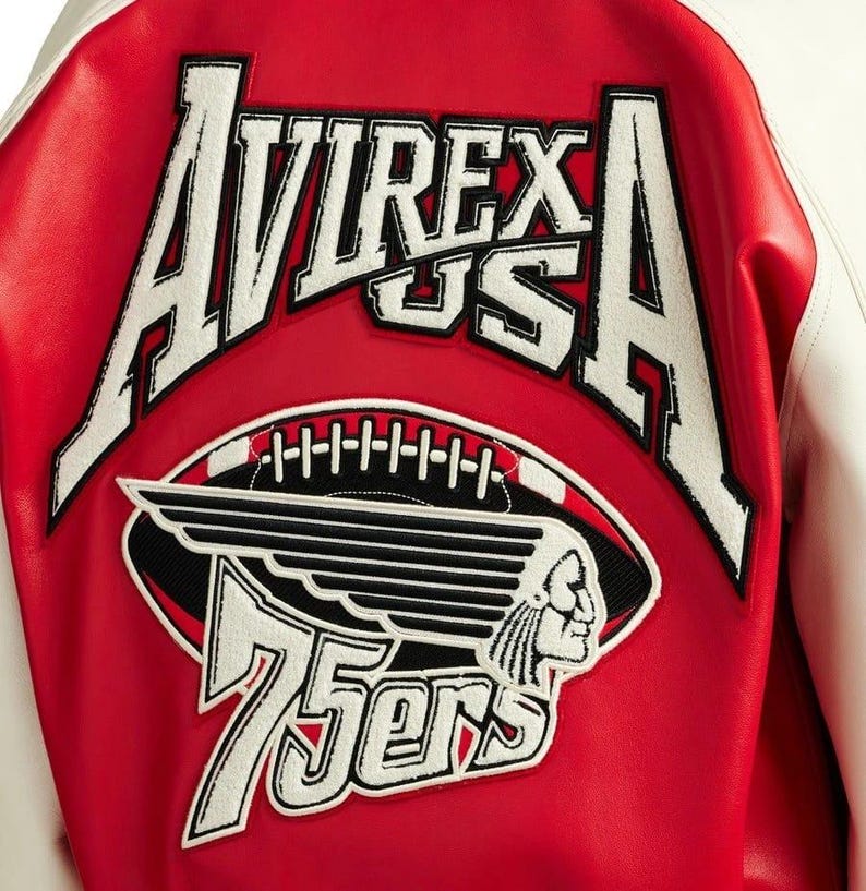Puede incluir: Chaqueta universitaria roja y blanca con el texto "AVIREX US A" en blanco. Debajo, un gr&aacute;fico de f&uacute;tbol con un perfil nativo americano y el texto "75ers". La chaqueta tiene un cuerpo rojo y mangas blancas.