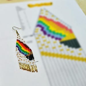 May include: A handmade beaded earring with a rainbow design and gold fringe. The earring features a white base with a colorful rainbow pattern and gold-colored beads at the bottom. The earring is displayed on a white surface.