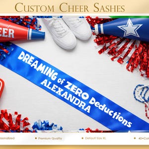 May include: A blue sash with white text reading "DREAMING of ZERO Deductions ALEXANDRA" is the focal point. Cheerleading accessories, including pom-poms, megaphones, and a foam finger, are arranged around the sash. The text "CUSTOM CHEER SASHES" is at the top of the image.