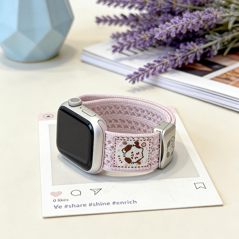 Front view of a pastel pink knit Apple watch band featuring a breathable hollow-out texture, an engraved metal slider, and a cute kawaii animal illustration patch, isolated on a white background.