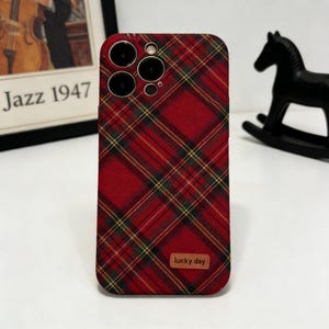 May include: A red plaid phone case with yellow and green accents. The case has a textured surface and a small brown label that reads "lucky day". The case has multiple camera cutouts.