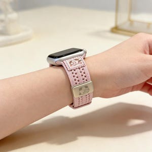 May include: A pink Apple Watch band with a woven design and a silver buckle. The band features a cartoon dog graphic on the band and buckle. The watch is silver.