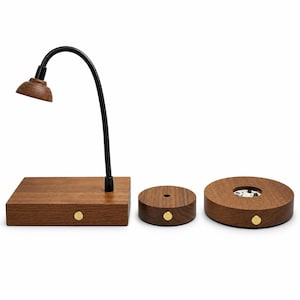 May include: A wooden desk lamp with a flexible black neck and a small wooden shade, alongside two circular wooden bases. Each wooden component features a small, round, gold-colored button on the front edge for operation and control.