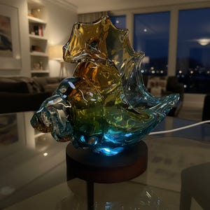 May include: A decorative glass sculpture in shades of blue, green, and amber, resembling a seashell. The art piece sits on a dark wooden base with a blue light emanating from beneath. The sculpture is displayed on a glass table.