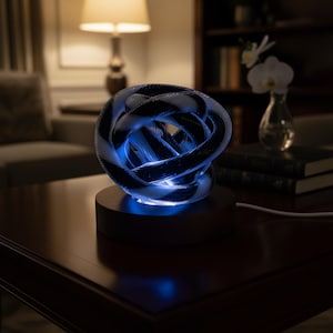 May include: A decorative, illuminated sculpture with a woven design. The sculpture is a sphere of interwoven black and white strands, lit with blue light from the base. It sits on a dark wooden base, creating a modern aesthetic.