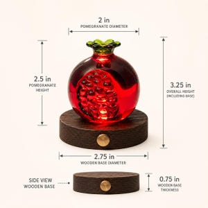 May include: A decorative glass pomegranate sculpture with a dark red hue, resting on a round wooden base. The pomegranate is 2.5 inches tall and 2 inches in diameter. The wooden base is 2.75 inches in diameter and 0.75 inches thick. Overall height is 3.25 inches.