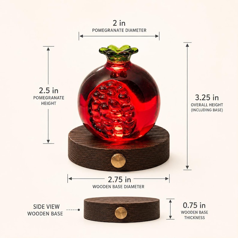 May include: A decorative glass pomegranate sculpture with a dark red hue, resting on a round wooden base. The pomegranate is 2.5 inches tall and 2 inches in diameter. The wooden base is 2.75 inches in diameter and 0.75 inches thick. Overall height is 3.25 inches.