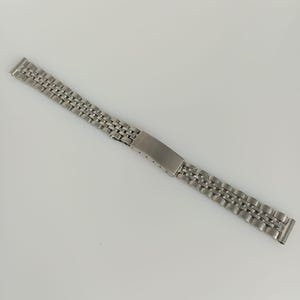 Op de afbeelding: Een zilverkleurige metalen horlogeband met een schakelontwerp bestaande uit kleine, afgeronde rechthoekige schakels. De band is voorzien van een centrale vouwsluiting met een glad, rechthoekig oppervlak en zichtbare gaatjes voor aanpassing.